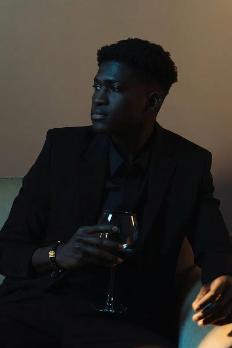 Homem de terno preto usando pulseira Supima preta com detalhes dourados