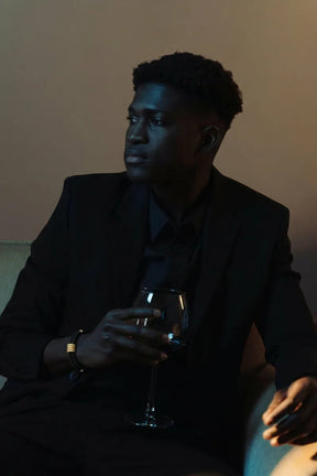 Homem de terno preto usando pulseira Supima preta com detalhes dourados